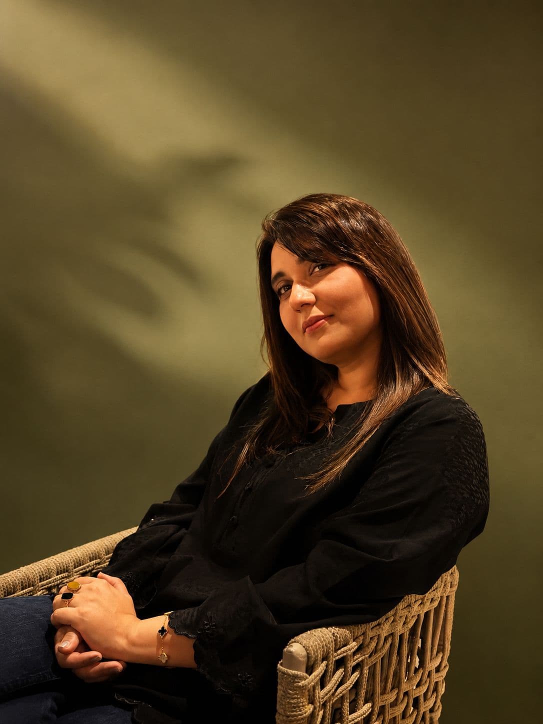 Aisha seated in a wicker chair against a green backdrop